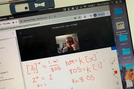 Photo of laptop showing equations written on a virtual whiteboard and student giving a thumbs up.