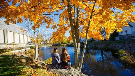 Two students sitting outside on campus in the fall.