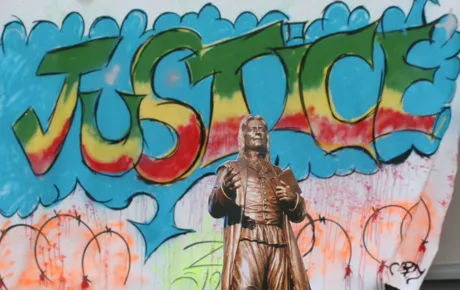 Little Roger mascot in front of social justice mural