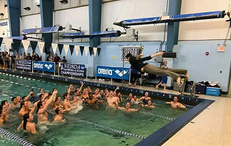 A student dives into a pool while his teammates celebrate their victory.