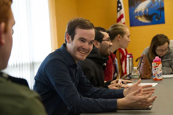 A student is sitting at a table listening to a conversation.