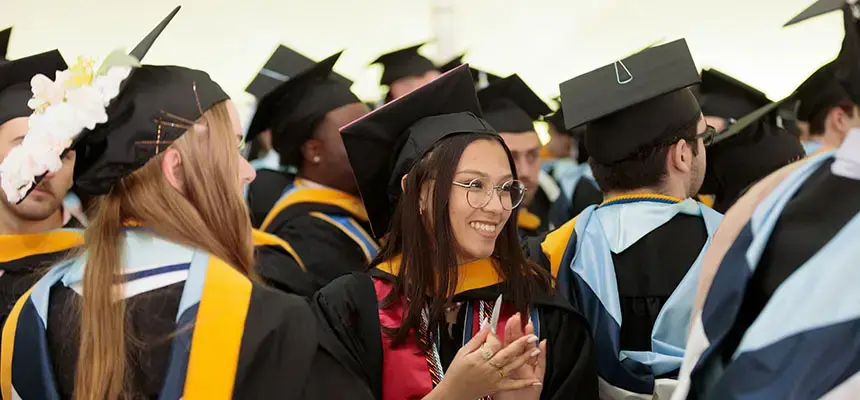 A graduate smiles at commencement wearing cap and gown