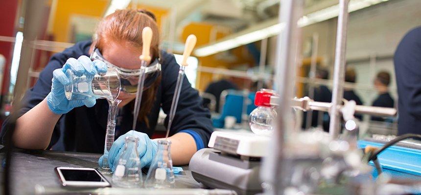 image of student wearing goggles carefully pouring liquid from a glass vessel in a lab on RWU's Bristol campus