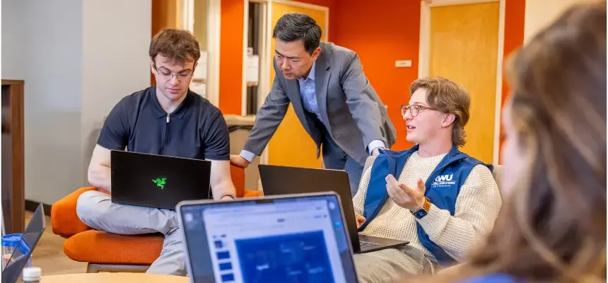 Graduate students and Dr. Wu sit together doing group work on laptops at our Providence Campus