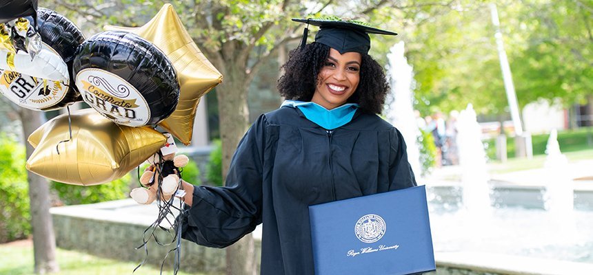 image of a smiling student wearing graduation robe and mortarboard holding her diploma and balloons at Commencement 2021 on RWU's Bristol campus