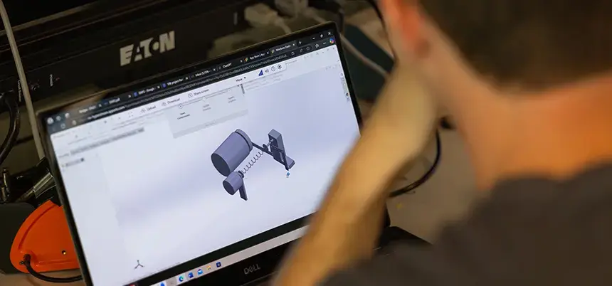 Looking over shoulder of a person at a laptop screen with a sketch of a contraption with a barrel and a spring