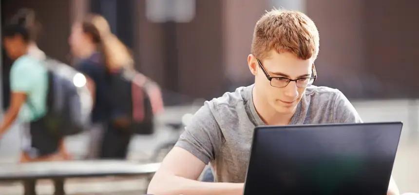 A young man works on a laptop outdoors