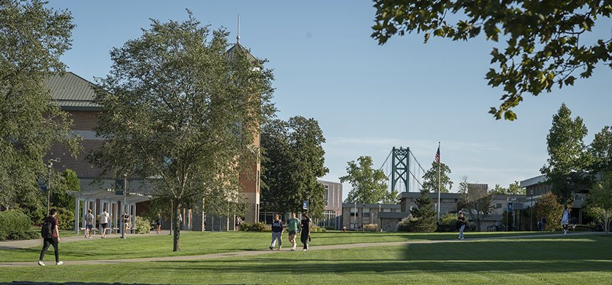 Students walk across RWU's Bristol Campus with Mount Hope Bridge and the American Flag in the background