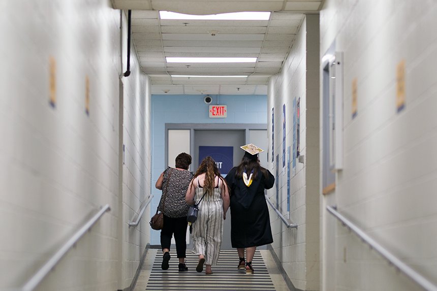 A 2020 graduate walks with family and friends down a hallway