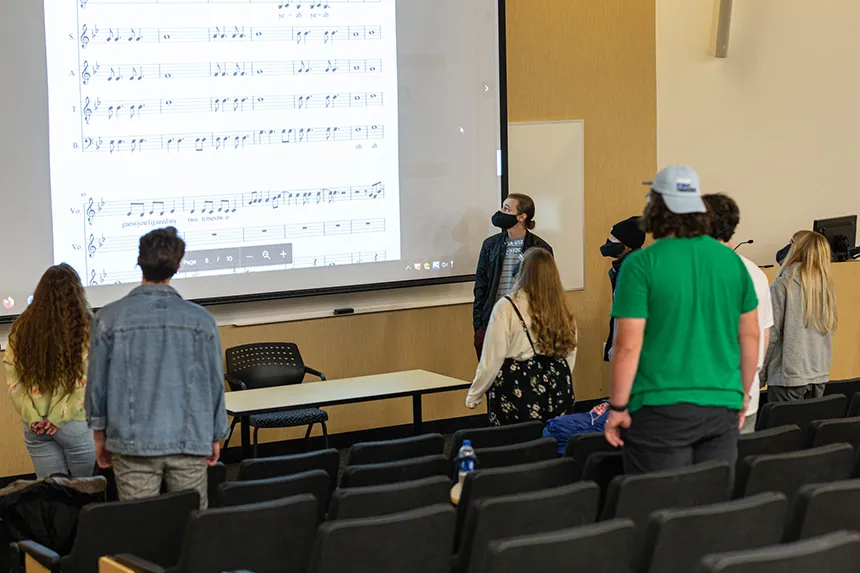 image of members of Hawkward following a musical score projected on the big screen during in-person rehearsal
