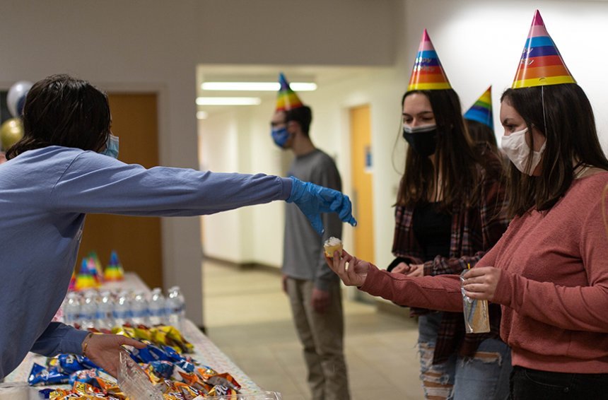 image of a masked student receiving a cupcake from another student wearing gloves