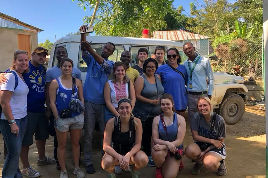 A group of people stand in front of a vehicle in a tropical country