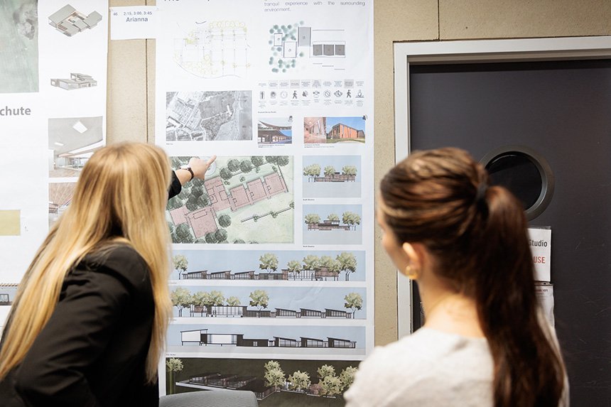 A photo of the backs of two people looking at an Architecture student's design on a poster