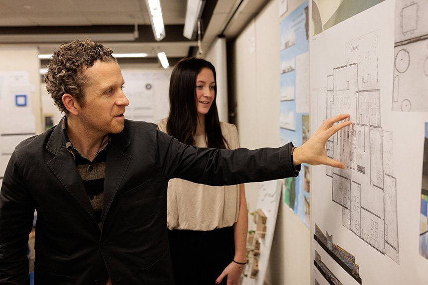 An Architecture alum points to a student's design on a poster as the student looks on