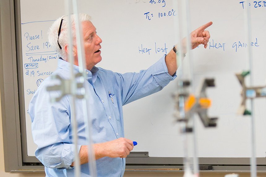 A biology professor pointing to a whiteboard 