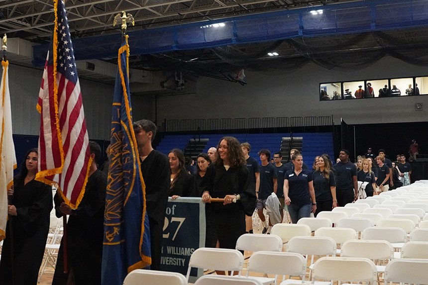 Students standing in an aisle between white chairs in the fieldhouse 