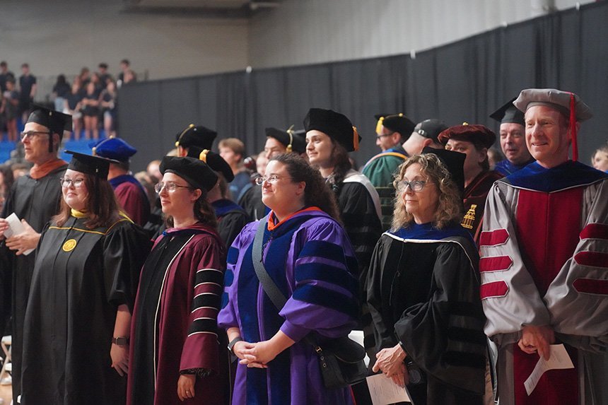 A group of faculty wearing their academic regalia standing and smiling 