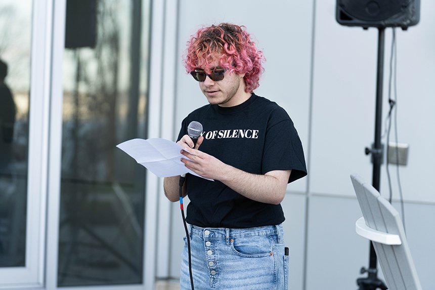 A student wearing a Day of Silence T-shirt speaks into a microphone. 