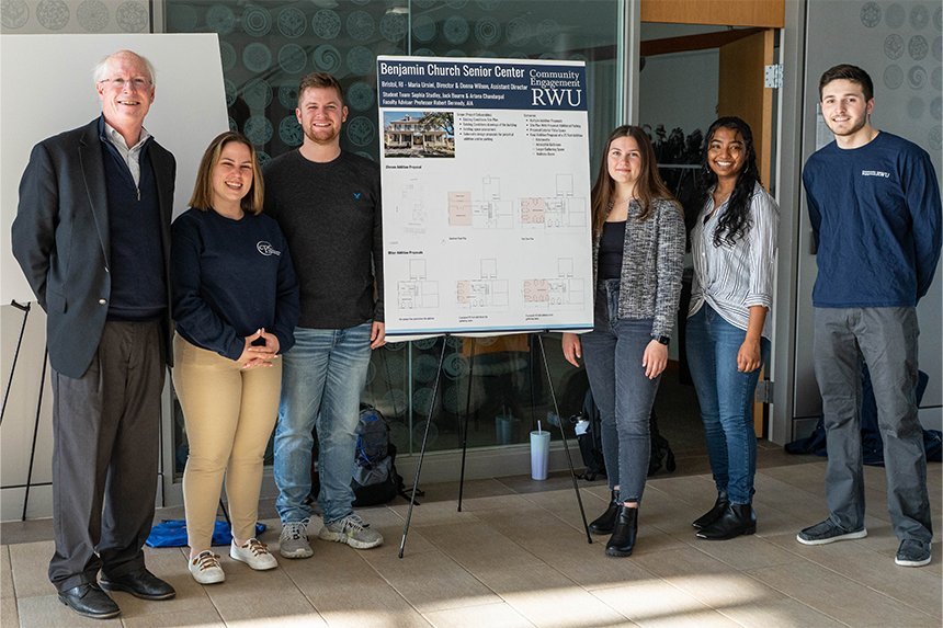 Students and a professor standing next to their poster presentation 