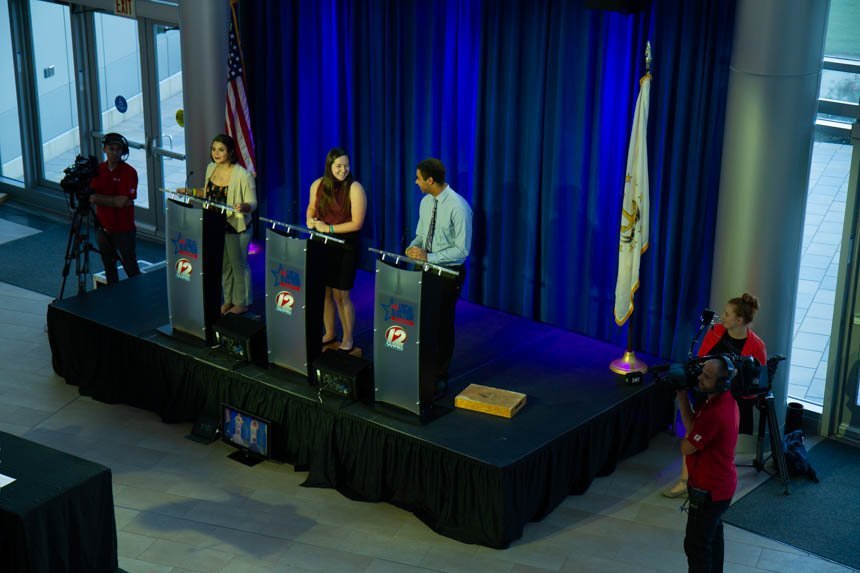 Students stand on stage at podiums. 