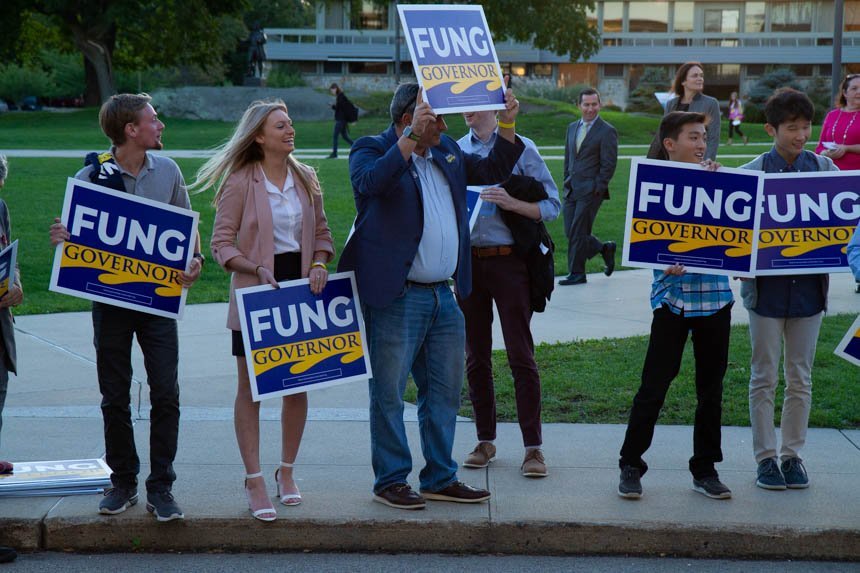 People stand on the sidewalk, raising signs that say "Fung."