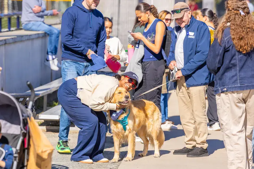 A Homecoming and Family Weekend attendee pets Roger, the First Dog, as President Yannis talks.