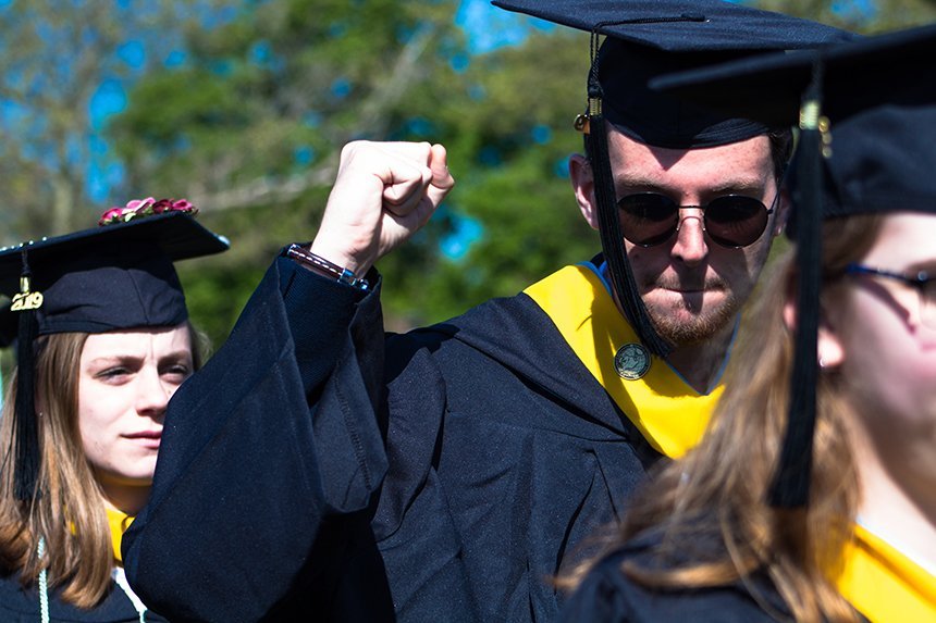 image of student celebrating graduation with a fist pump in cap and gown