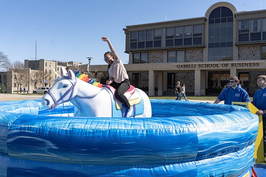 A student rides a mechanical unicorn on the green in front of the library as part of Queer Fest.