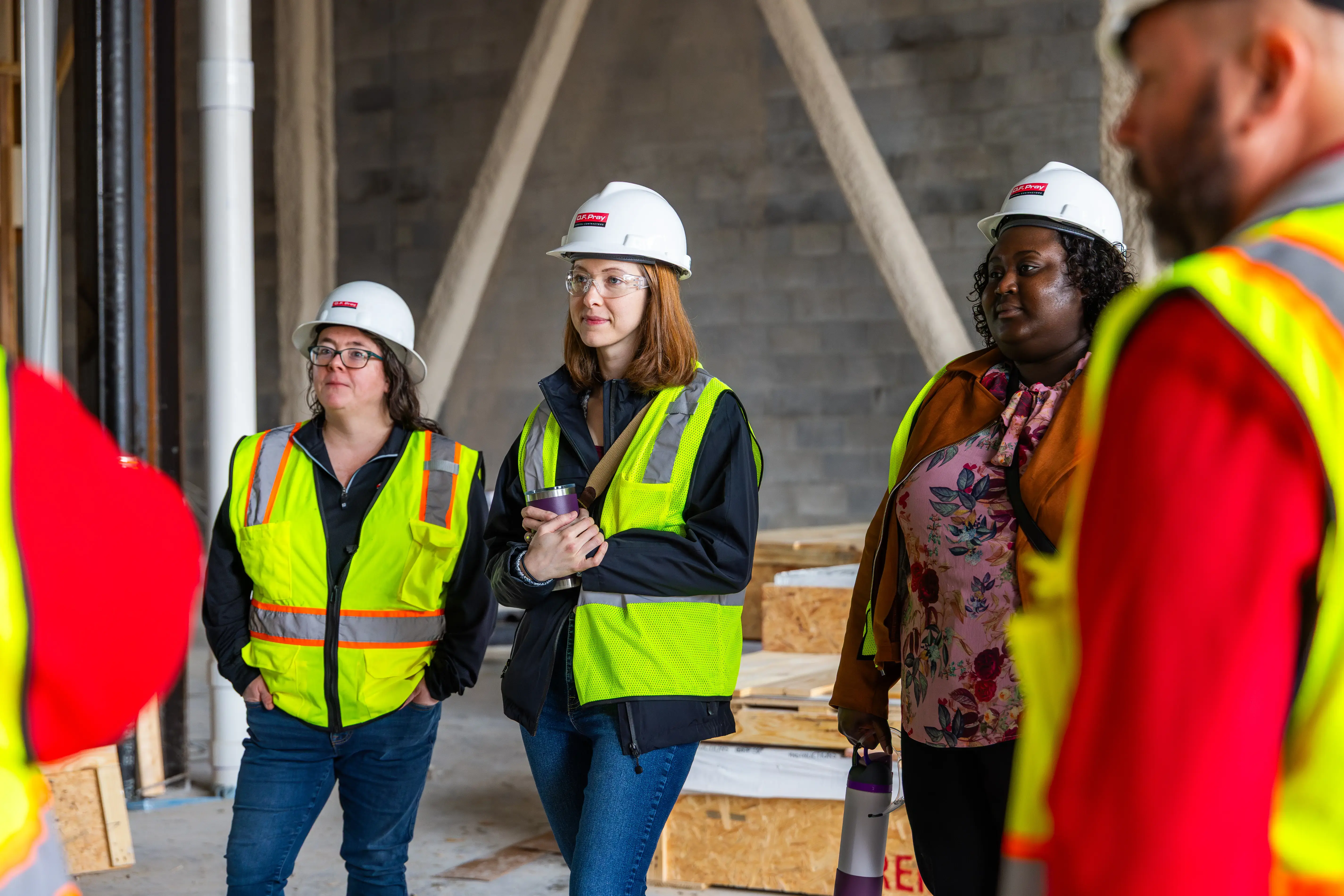 Group of construction workers in safety vests and hard hats listening during a site visit inside a partially built structure.