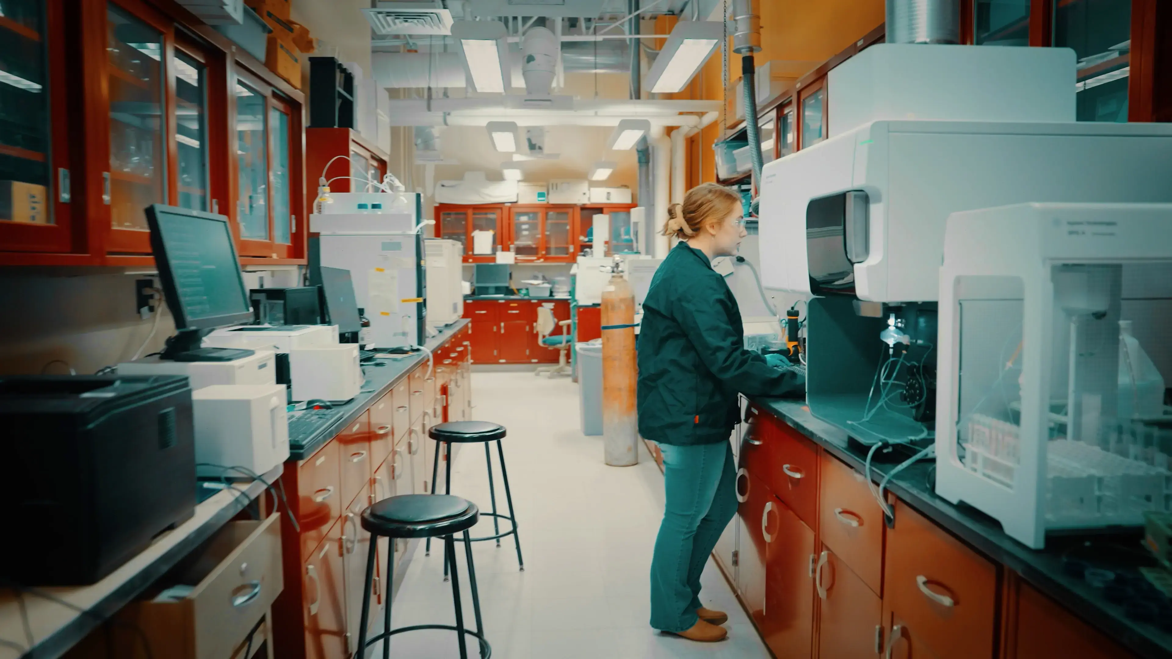 Researcher operates analytical instrument in a bright chemistry lab lined with computers and equipment. 