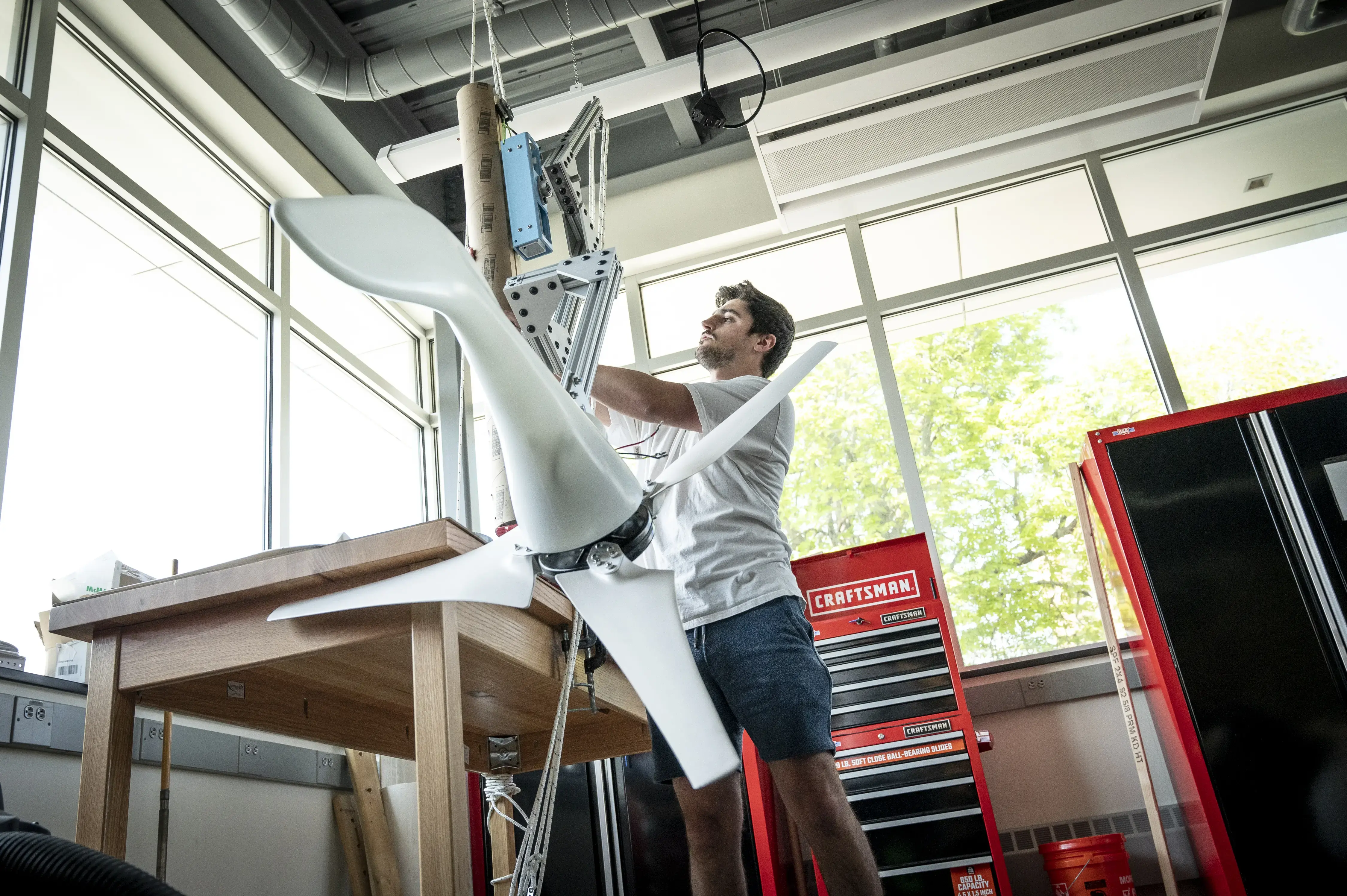 Student works on a wind turbine project in a bright engineering lab with tools and equipment nearby.