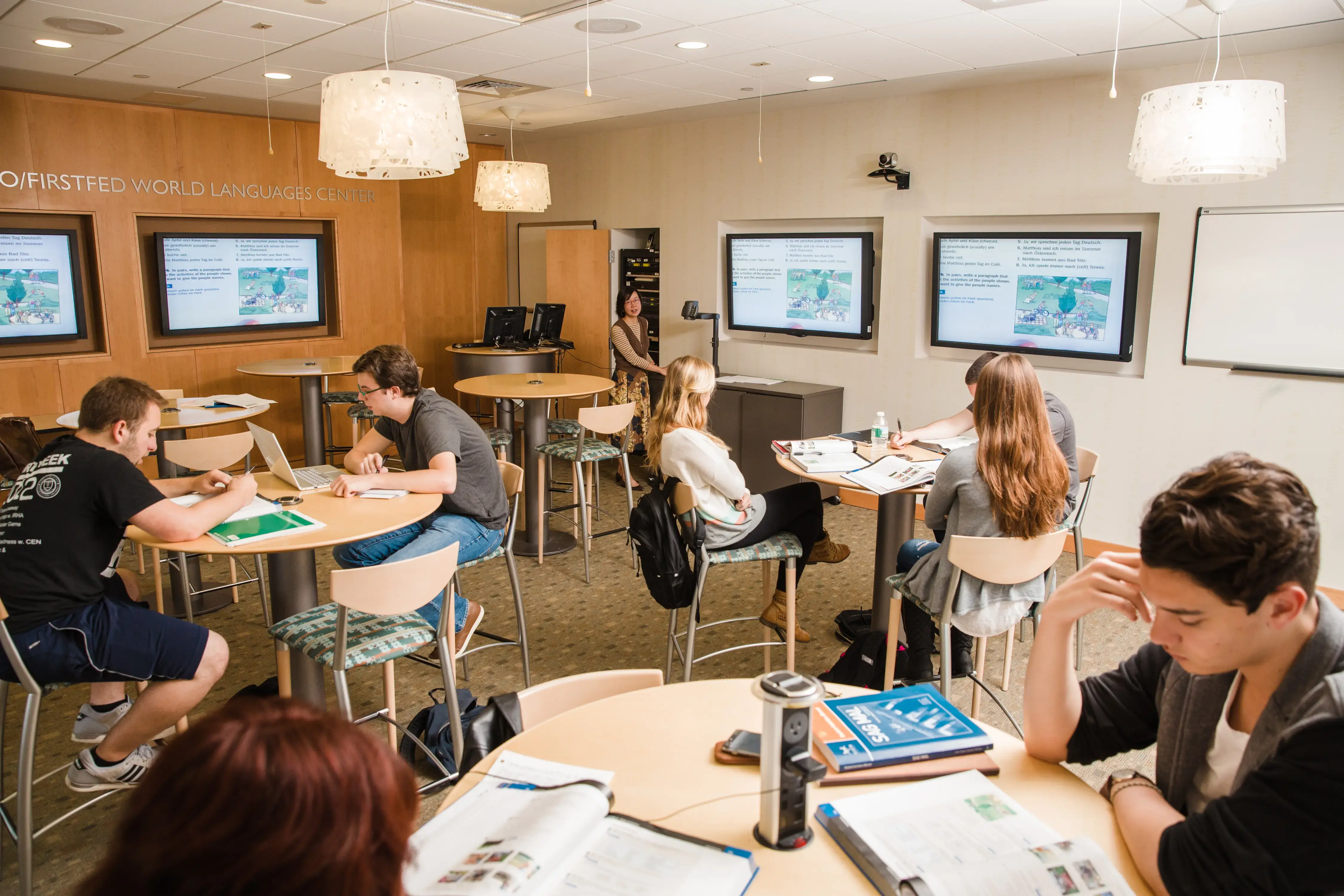 Students working in small groups in a modern language lab with screens displaying educational content.