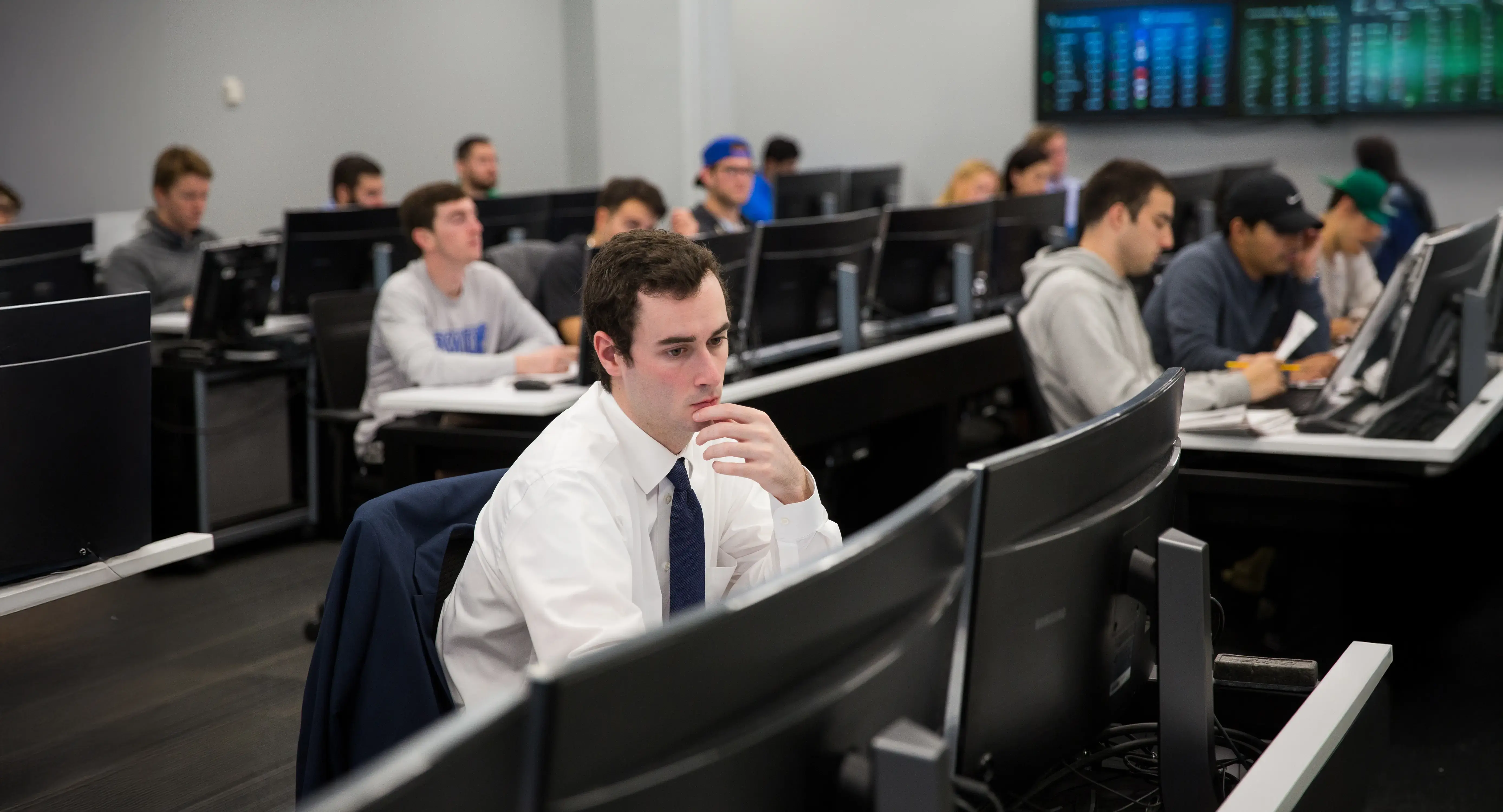 Students work at computer stations in an Economics classroom, analyzing data displayed on large monitors.