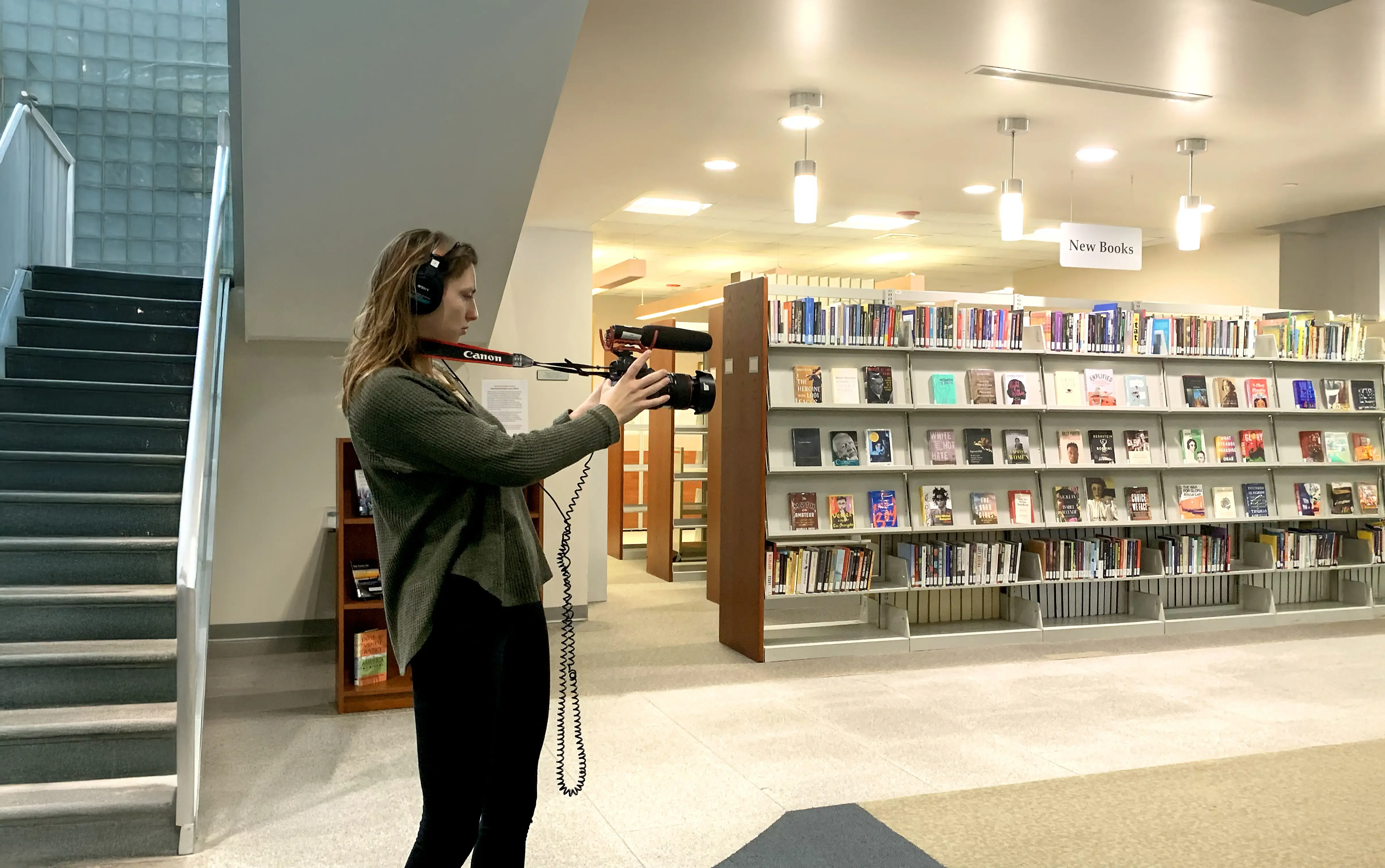 A student journalist records video with a Canon camera and microphone in a library.