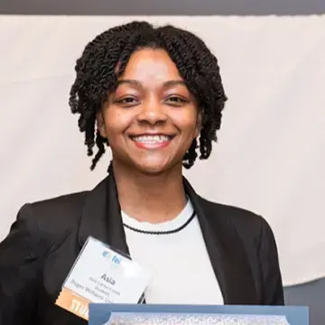 Student in a blazer smiles while holding an award, wearing a name badge at a Roger Williams University event.