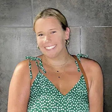 Student in a green polka dot dress smiles in front of a stone wall.