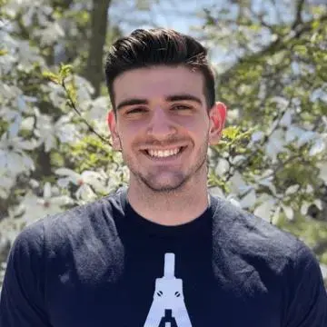 Student smiling outdoors in front of flowering trees on the Roger Williams University campus.