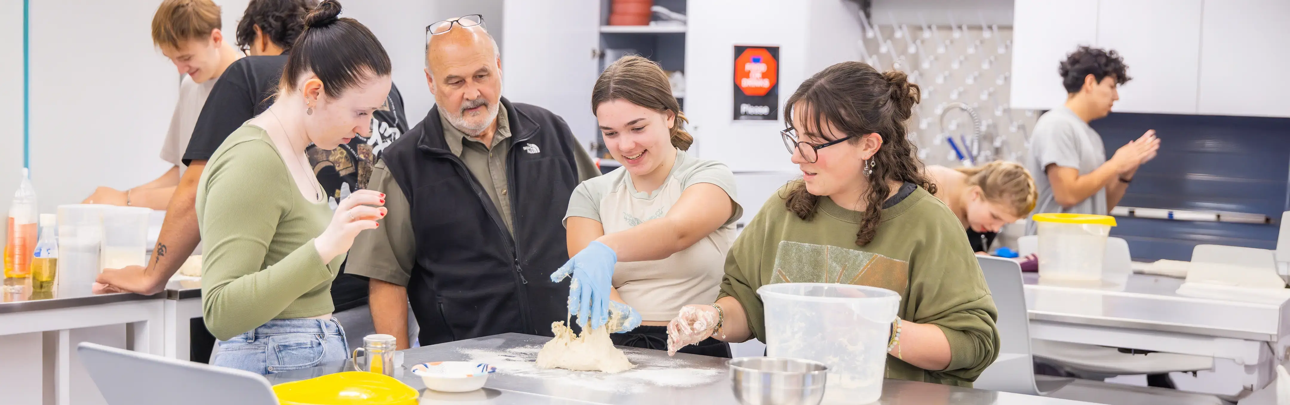 Students and an instructor smile while working with dough in the Food Science Lab.