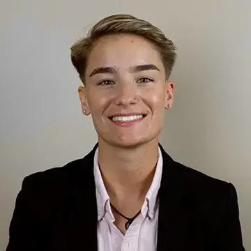 Student in a blazer and light shirt smiles in front of a neutral background.