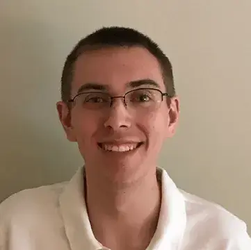 Student in glasses and a white collared shirt smiles in front of a neutral background.