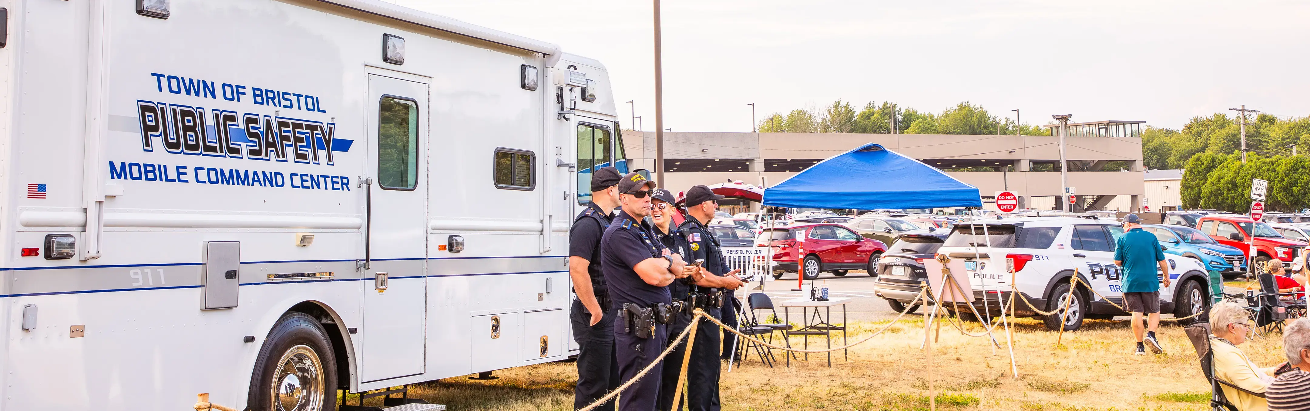 Public safety officers stand near a Mobile Command Center at an outdoor community event with tents and vehicles. 