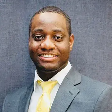 Student in a gray suit and yellow tie poses for a professional portrait against a dark background.