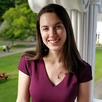 Student in a maroon dress smiles while standing outdoors near a white column.