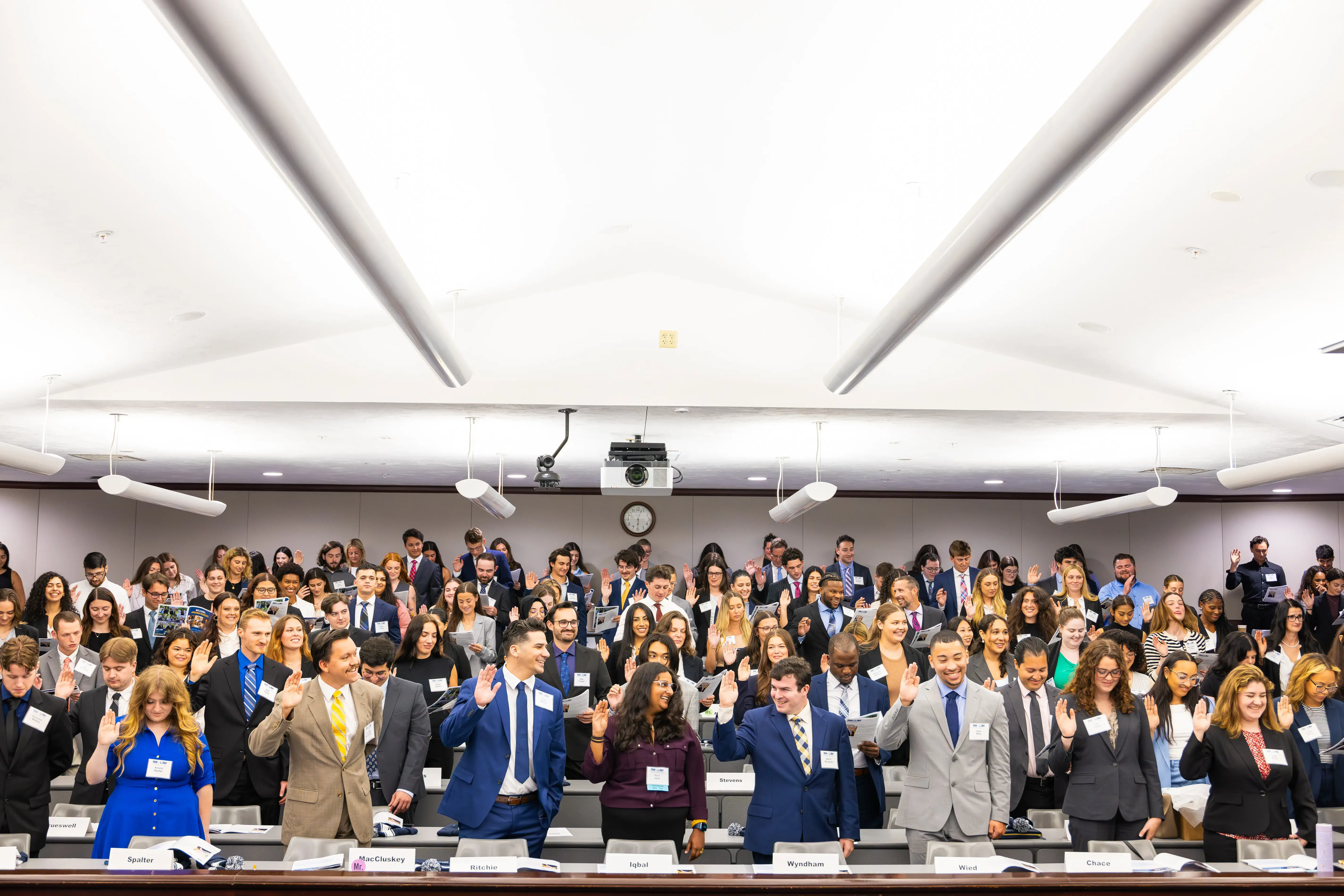 Law students raise hands and stand at law orientation