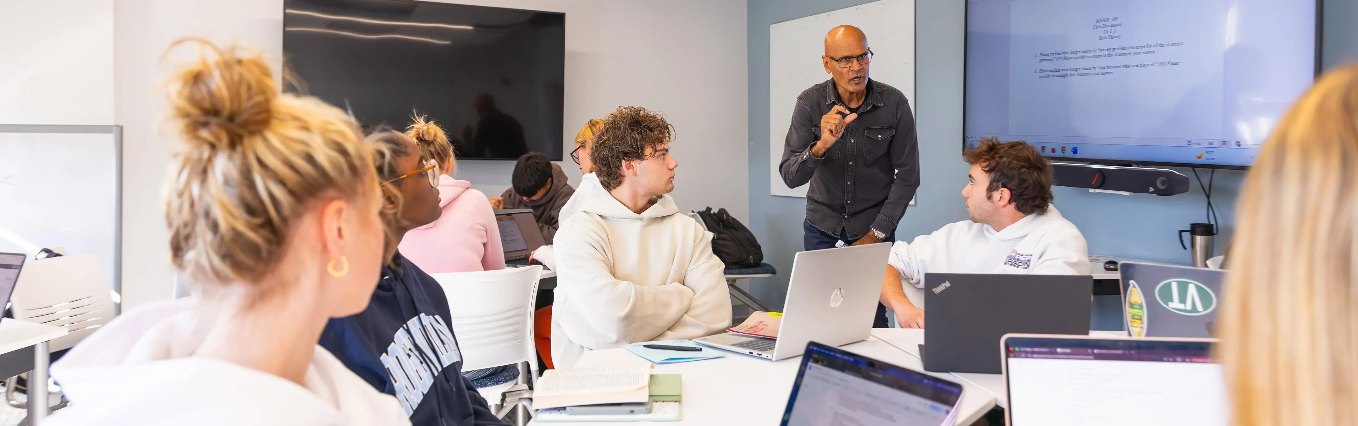 A professor intensely lectures to students in a bright classroom.