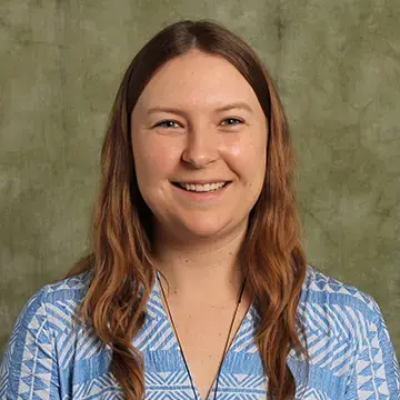 Student in a blue patterned blouse smiles in front of a green studio backdrop.