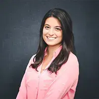 Alumna in a pink blouse smiles in front of a dark background for a professional headshot.