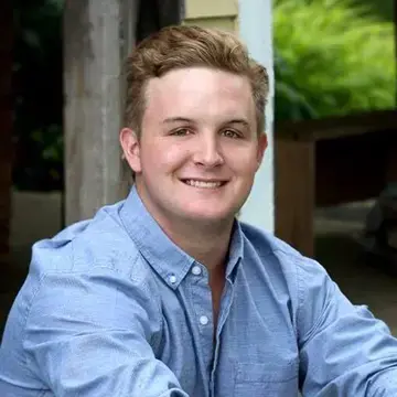 Student in a blue button-down shirt smiles in an outdoor portrait.