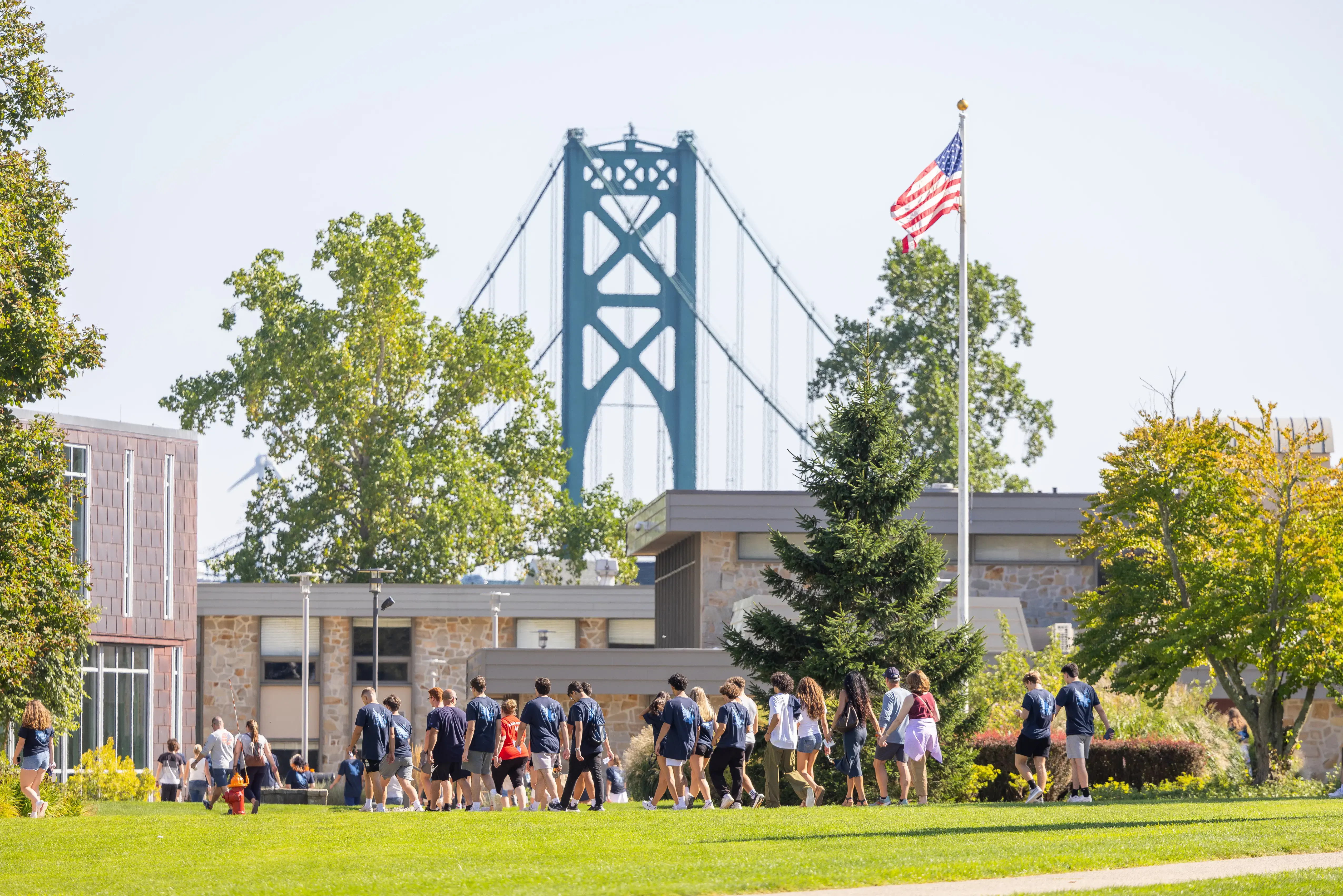People walk across campus with Mount Hope Bridge in the background