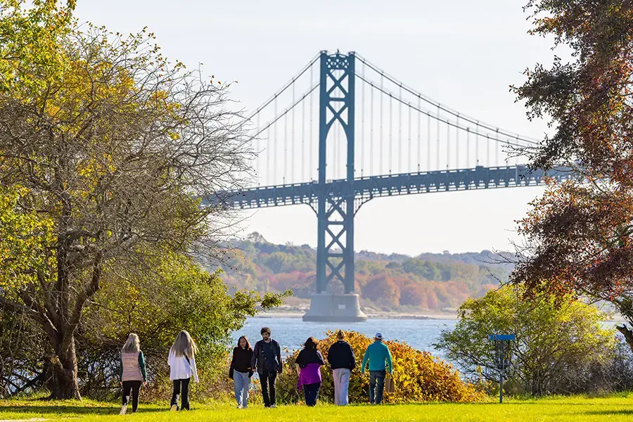 People walk on campus in front of Mount Hope Bridge
